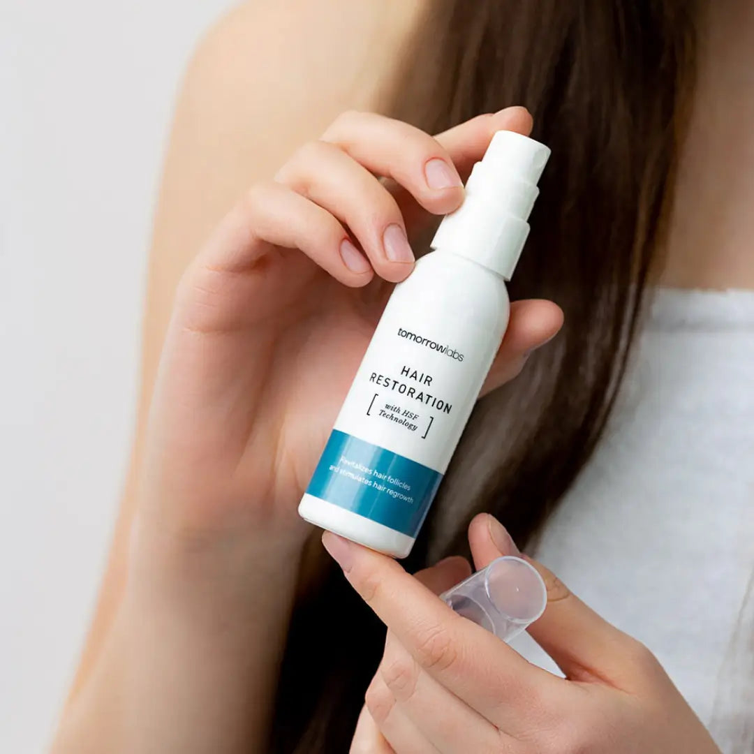 Person holding a 50ml bottle of Tomorrowlabs Hair Restoration Liquid, supporting hair regrowth and strengthening thinning hair at the root.
