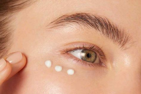 Close-up of a woman applying eye cream, showcasing eye care routine to reduce puffiness and dark circles.