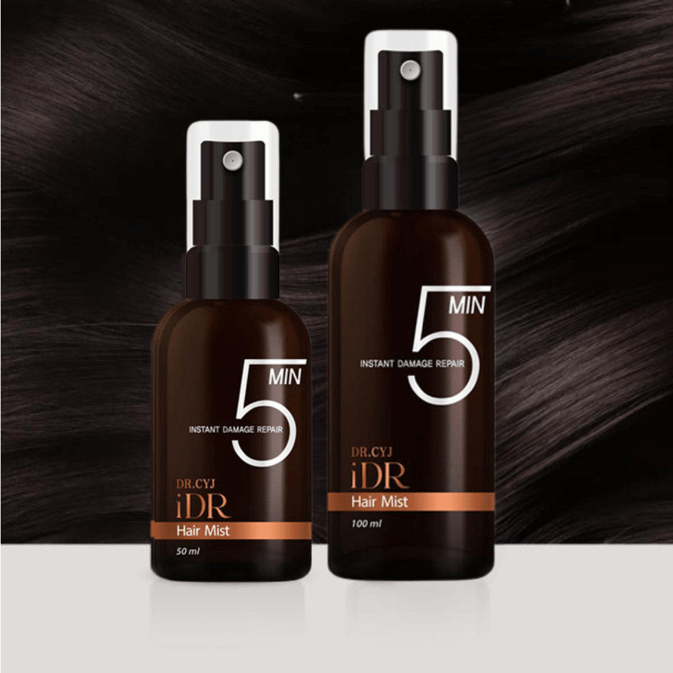 Two bottles of Dr. CYJ iDR Hair Mist in 50 ml and 100 ml, dark amber bottles with white spray heads and orange design details, presented against a glossy black hair background.