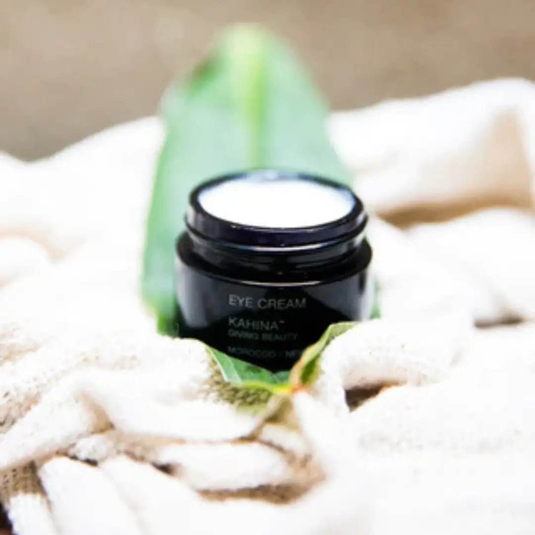 Close-up of Kahina Eye Cream open jar beside aloe leaves, showcasing its creamy texture and natural ingredients for soothing under-eye care.