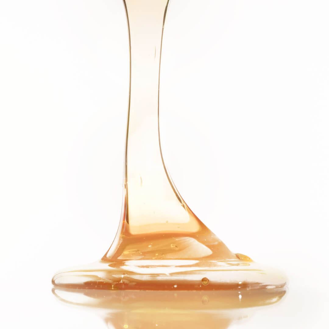 Viscous honey-like liquid dripping, symbolizing natural ingredients used in Leonor Greyl Bain Traitant a la Propolis shampoo for soothing dandruff.