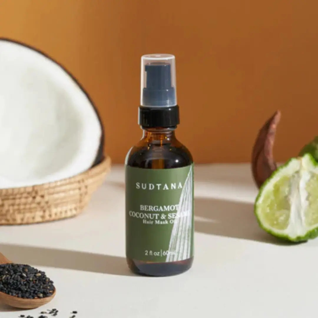 Sudtana bergamot, coconut & sesame hair oil displayed with coconut and sesame seeds, promotes hair health.