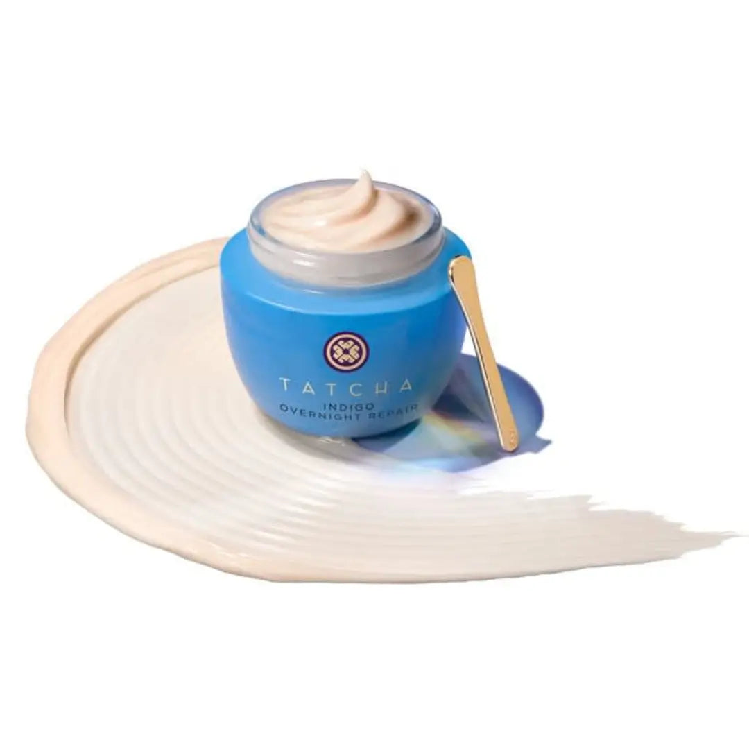 Open jar of Tatcha Indigo Overnight Repair cream showing creamy texture, includes spatula for application.