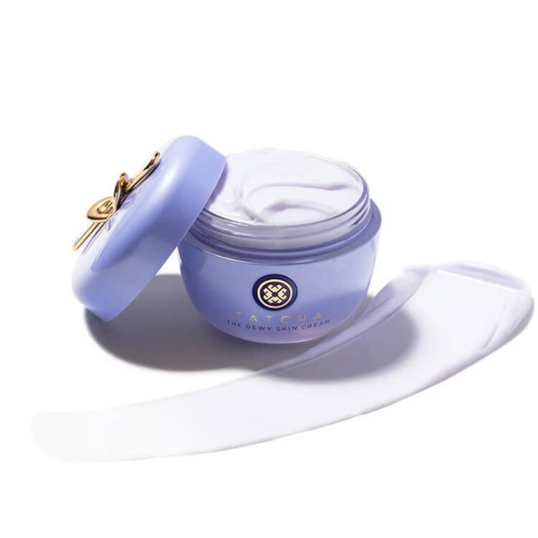 Open lavender container of Tatcha The Dewy Skin Cream, showcasing its creamy texture and built-in gold spatula on the lid.