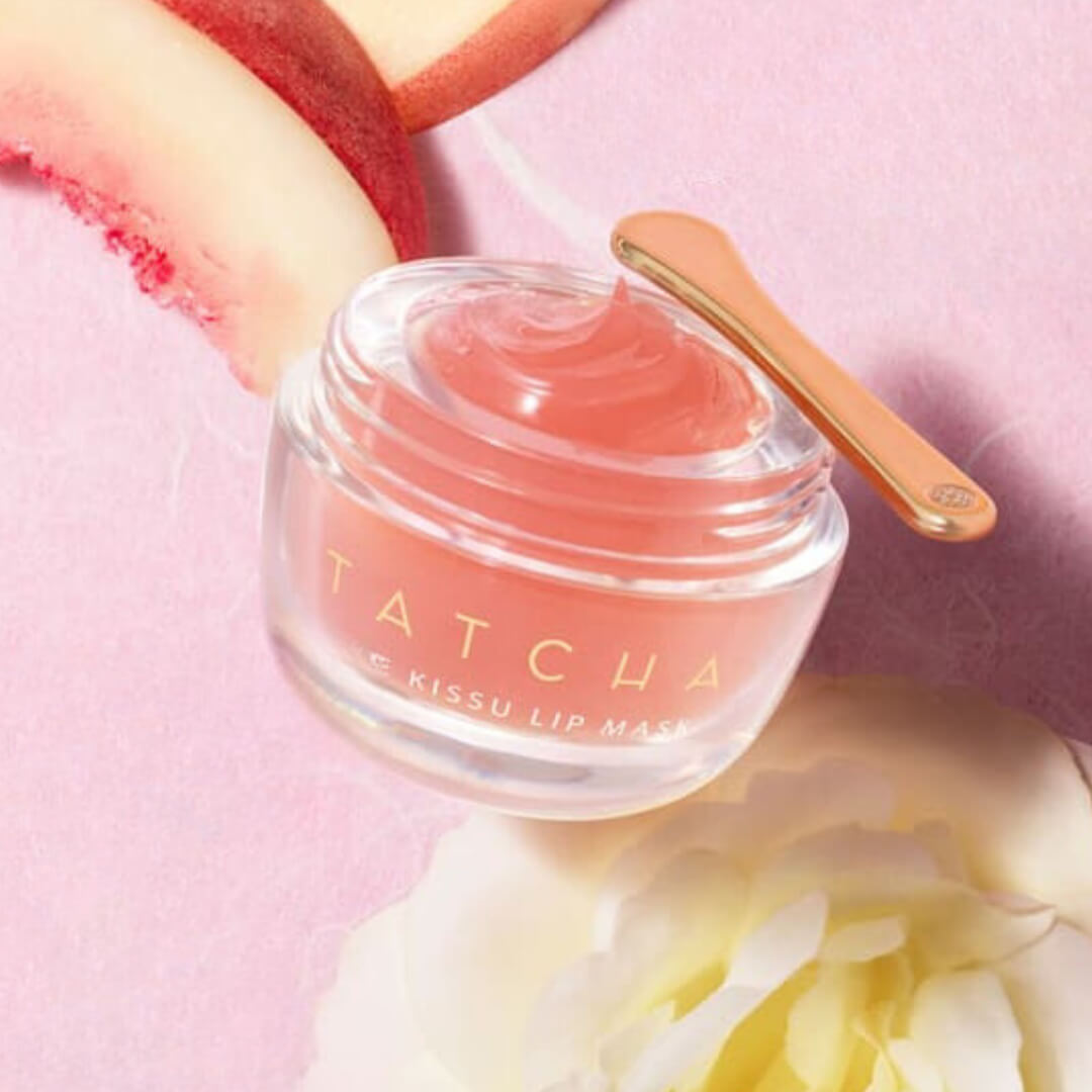 Tatcha The Kissu Lip Mask displayed with a gold spatula on a pink background, highlighting its luxurious jelly texture.