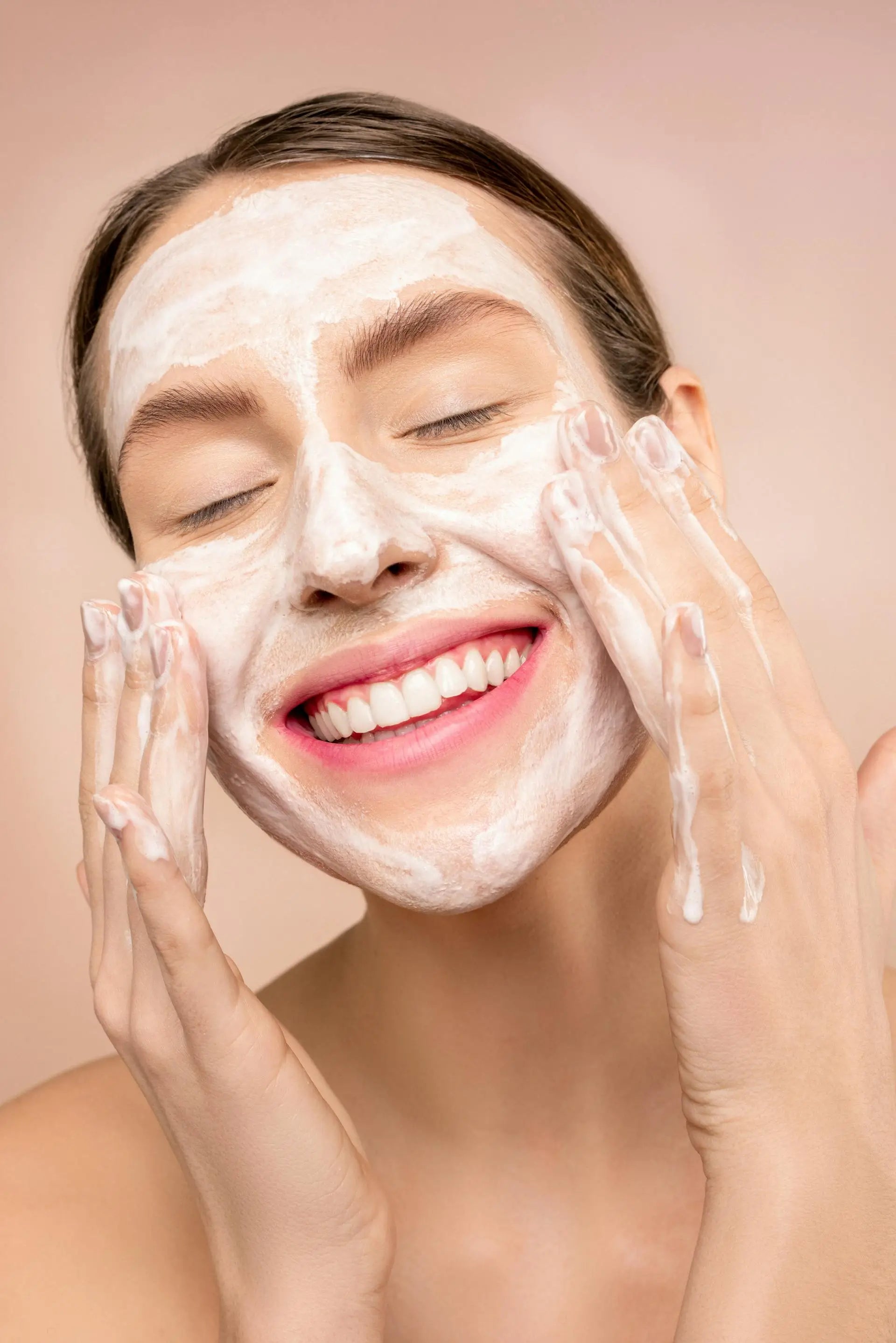 Woman smiling and applying face cleanser, demonstrating face care routine for healthy, glowing skin.